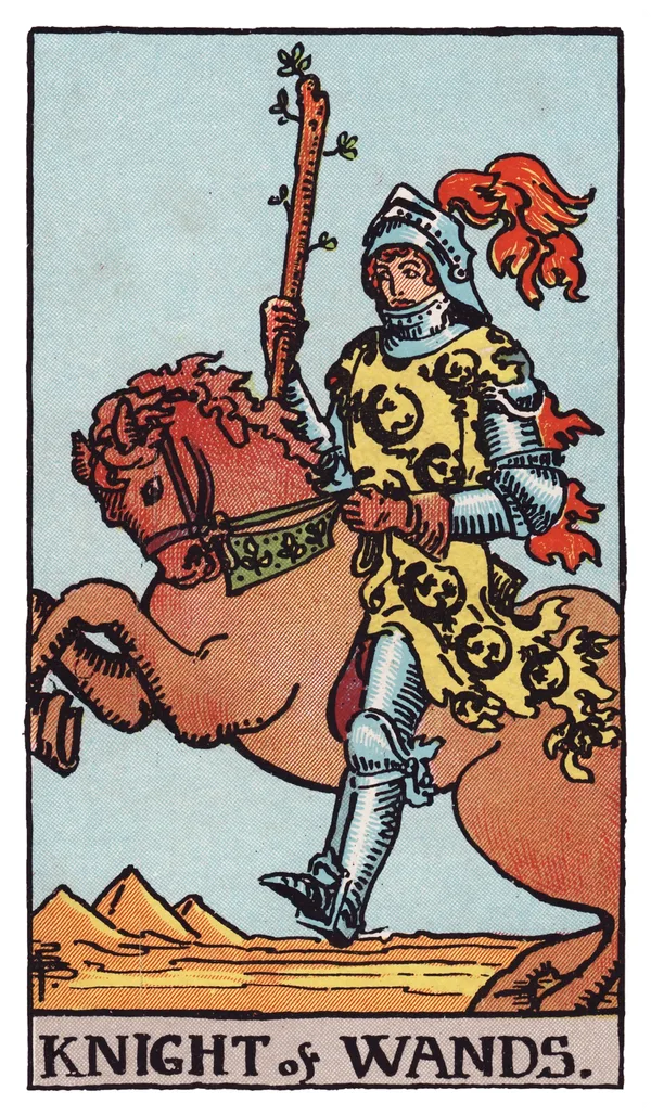 The Knight of Wands from the Rider-Waite-Smith deck: an armored knight on a rearing chestnut horse charges forward across a desert landscape, holding a budding wand aloft, his tunic and the horse's caparison patterned with salamanders, three pyramids visible in the distance.