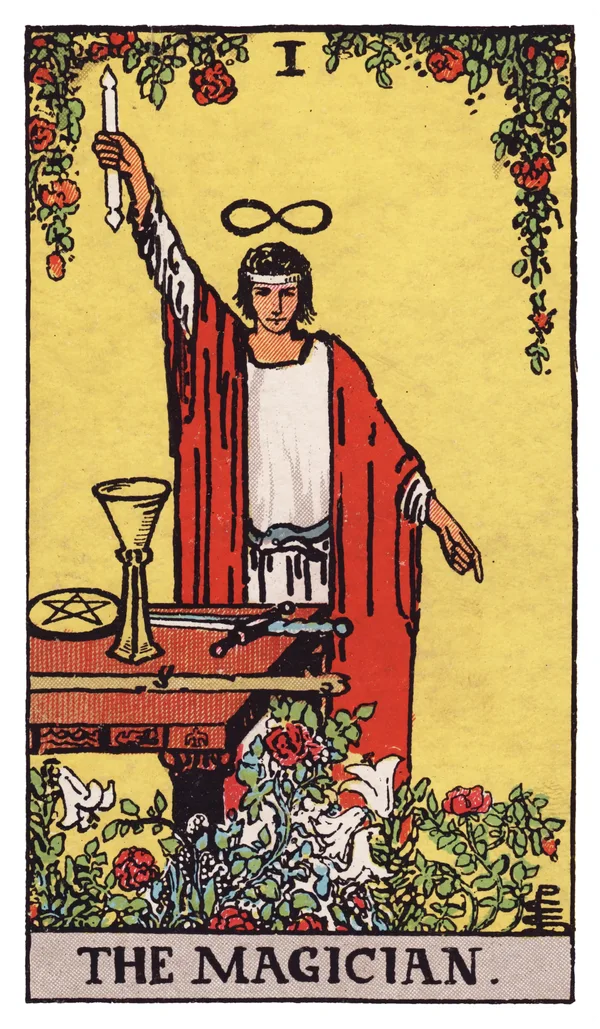 The Magician from the Rider-Waite-Smith deck: a young man in a white robe under a red cloak stands behind a table, right arm raised holding a wand toward the sky, left hand pointing down toward the earth, a lemniscate (infinity symbol) floating above his head, an ouroboros serpent belt at his waist, and a cup, pentacle, sword, and wand — the four Minor Arcana suit symbols — arranged on the table before him, with red roses and white lilies growing at his feet.