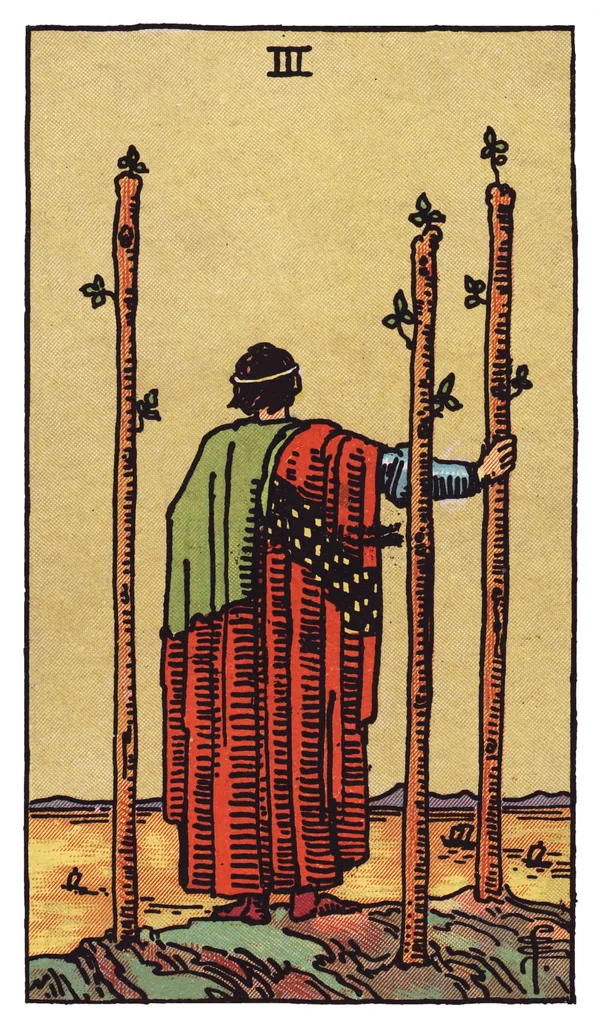 The Three of Wands from the Rider-Waite-Smith deck: a robed figure stands on a cliff edge with his back to the viewer, watching ships sail across the sea below, three tall wands planted firmly in the ground around him, one gripped lightly under his hand.